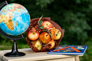 Back to school time. Copy space image for russian Day of Knowledge. Bright autumn image. Globe, fruit bouquet and textbook. Bouquet for teacher. Selective focus.