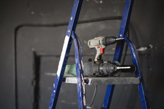 Perforator drill and handheld screwdriver on the stepladder background.