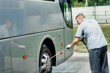 Male driver washes large bus on summer day at open car wash. Service or service for washing large...