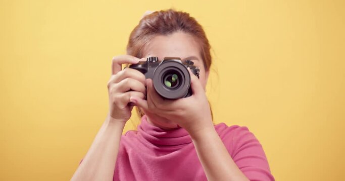 Brunette young Asian woman happy and joyous, smiling proudly with a digital camera and isolated yellow background. Travel concept.