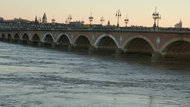 Bridge with a raging river un a sunset with an orange background , and streetlight silhouettes in budeaux, france. Static shot.