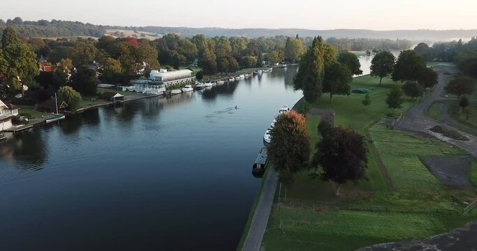 Peaceful sunrise drone shot of a single rower on the river in Henley-on-Thames, Oxfordshire. The clip starts far away from the rower, revealing the beautiful landscape, and slowly flys closer.