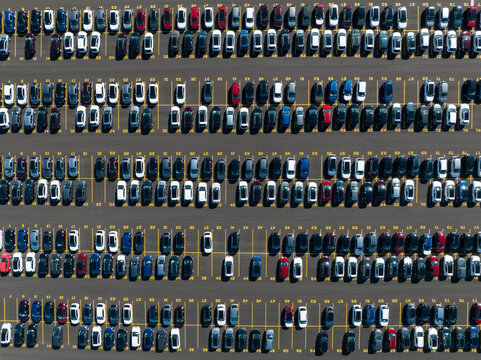 A direct overhead aerial view above a parking lot of newly manufactured cars, outside of a manufacturing plant.
