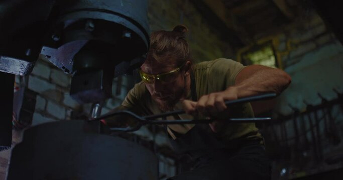 concentrated smith is working with pneumatic forging hammer in forge, tilt up portrait, 4K, Prores