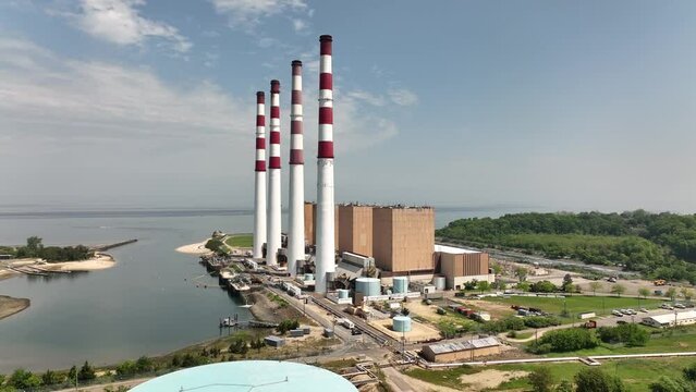 An aerial view of the largest power generation facility on Long Island. Taken on a sunny day with blue skies. The camera dolly in and pan left towards the red and white stacks on the facility.
