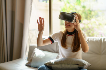 Smiling Asian woman having fun using VR glasses playing game at home happily and enjoy virtual reality.