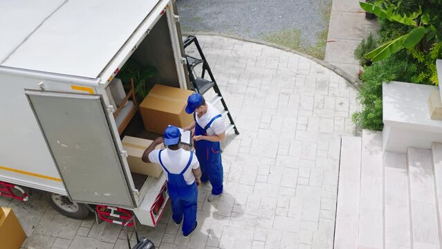 Workers unloading boxes from van outdoors.House move, mover service and Moving service concept.Two young handsome smiling workers wearing uniforms are unloading the van full of boxes.