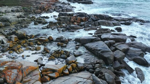 Aerial shot above a  section of the Orange coloured boulders of the Bay of Fires