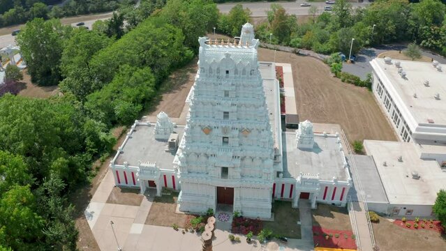 Aerial drone rotating shot of white hindu south Indian temple along the side of the road at daytime.