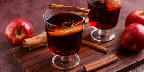 Glasses of tasty mulled wine, apples and cinnamon on color background