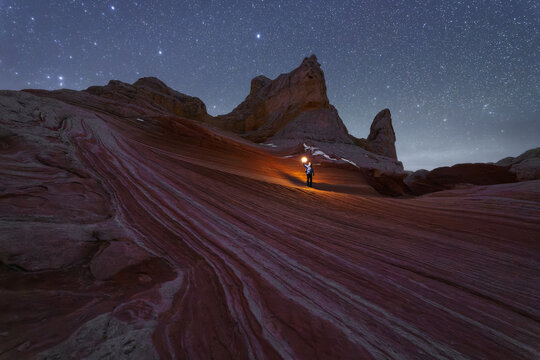 Traveler with flashlight on rock formation at night
