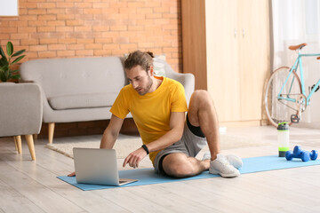 Sporty young man using laptop for online training at home