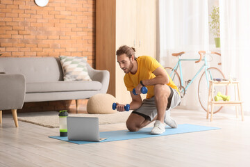 Sporty young man using laptop for online training at home