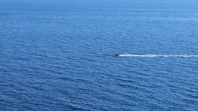 Small boat driving at high speed on the deep blue ocean. RIB boat on the ocean. Boat driving right to left on the dark blue sea. Inflatable boat with an outboard motor. 