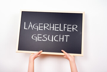 Zwei Arme halten eine Tafel hoch auf der LAGERHELFER GESUCHT steht