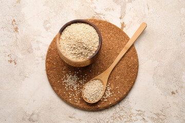 Cork mat with bowl and spoon of sesame seeds on light background