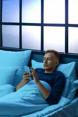 Young man using mobile phone in bedroom at night