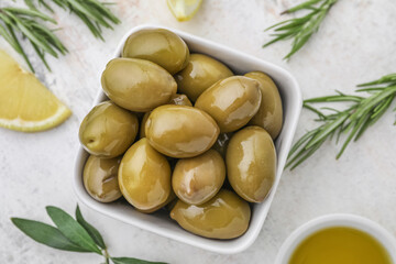 Bowl of tasty green olives on light background, closeup