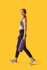 Young woman with purple foam roller on yellow background