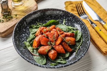 Plate of tasty baked carrots with greens on light wooden table, closeup