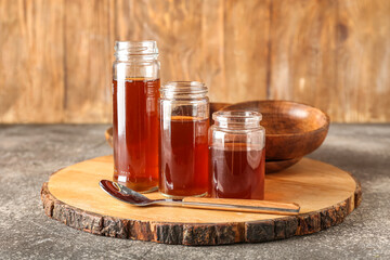 Wooden board with jars of maple syrup on table