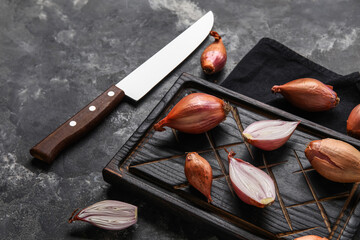 Wooden board with fresh onion and knife on dark background, closeup