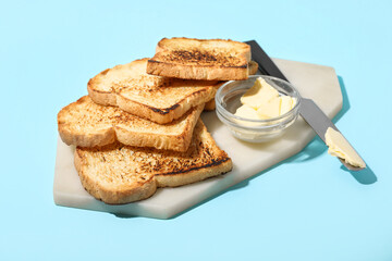 Board with toasts, bowl of butter and knife on color background
