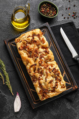 Wooden board with tasty Italian focaccia, jug of oil and peppercorns on dark background