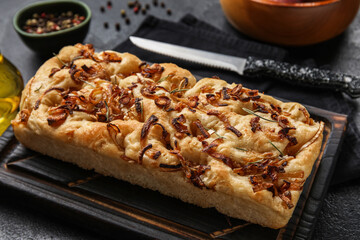 Wooden board with tasty Italian focaccia on dark table, closeup