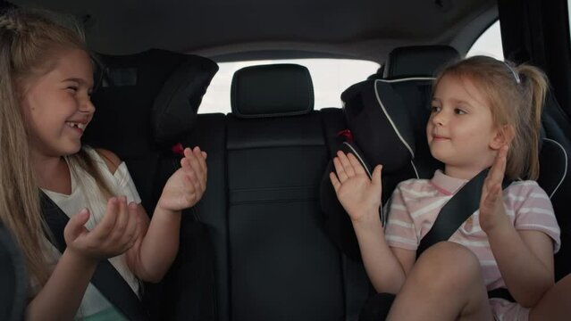 Two caucasian female children sitting on the back seat and playing clapping game. Shot with RED helium camera in 8K.