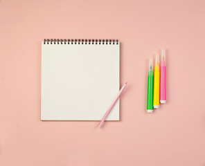 Notepad with white sheets and a pen and markers on a pink background