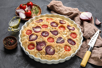 Baking dish with delicious Italian focaccia and ingredients on dark background