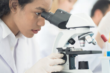 Close up woman scientist looking through microscope doing analysis for germs and bacteria of test sample in the laboratory. Female specialist working with biotechnology research with microscope