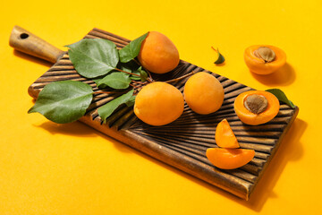 Wooden board with ripe apricots and leaves on color background