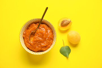 Bowl of tasty apricot jam on yellow background