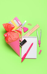 School cone with stationery supplies on green background