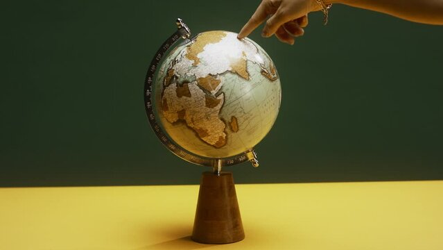 A spinning globe on a table, a finger pointing at destinations, green and yellow background