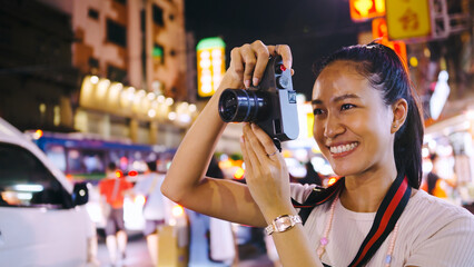 An Asian female tourist enjoys taking photos of the night view of Yaowarat Road or Chinatown in Bangkok, Thailand.
