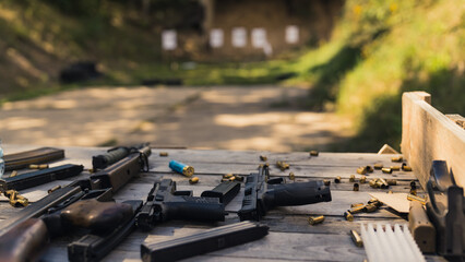 Numerous guns, rifles, and ammunition bullets placed on a wooden table near the shooting range....