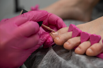 The master makes a pedicure applies pink polish on the nails. 