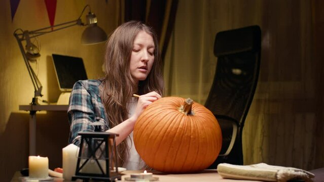 Preparing pumpkin for Halloween. Woman sitting and marking pumpkin with pencil before carving halloween Jack O Lantern at home for her family.