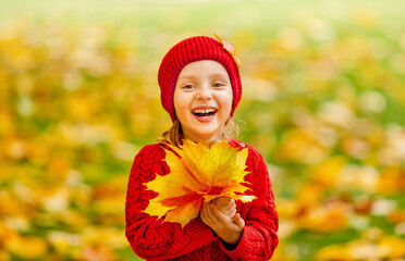 Naklejka premium a smiling in red knitted clothes child is having fun with fallen autumn leaves