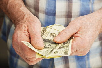 Close-up of an senior man's hands holding money 100 dollar bills.