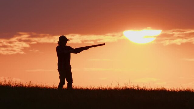 Silhouette of hunter takes aim with shotgun against the sunset sky. Side view.