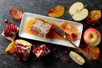  Honeycomb, apples, and pomegranate on a black stone table.
