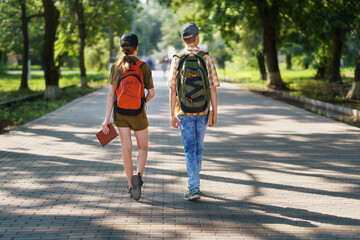 portrait of students in a city park, teenage schoolchildren a boy and a girl walking along a path, rear view