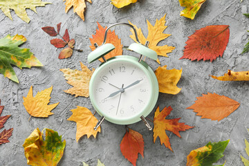 Autumn leaves and alarm clock on gray textured background