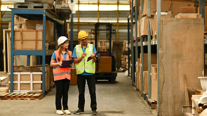 Full length of female managers and worker checking inventory in a warehouse with shelves full of cardboard boxes in the background