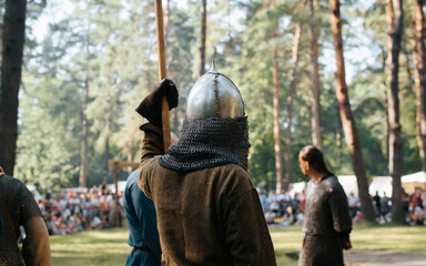 Rear view of an unrecognizable knight warrior in helmet and with spear standing in forest. Festival of historical reconstruction of Middle Ages in open air