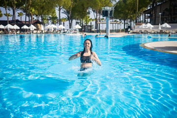Naklejka premium Young brunette teen girl jumping to a blue swimming pool in a hotel in Turkey. Having fun at vacation